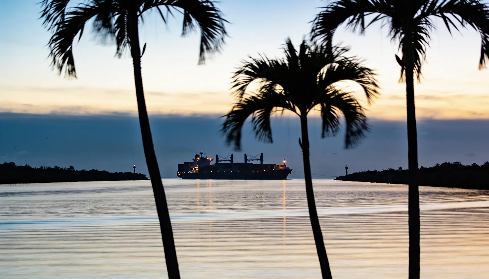 A container ship leaving a South Florida port at dusk